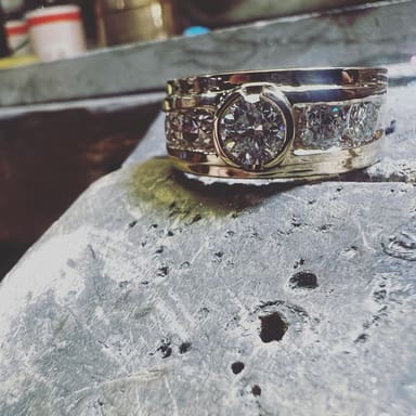 The ring with its stones set, photographed close up with the bench and tools behind it.